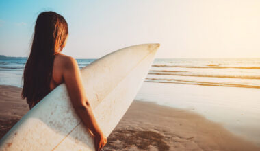 Image of a teen staring at the ocean holding a surfboard