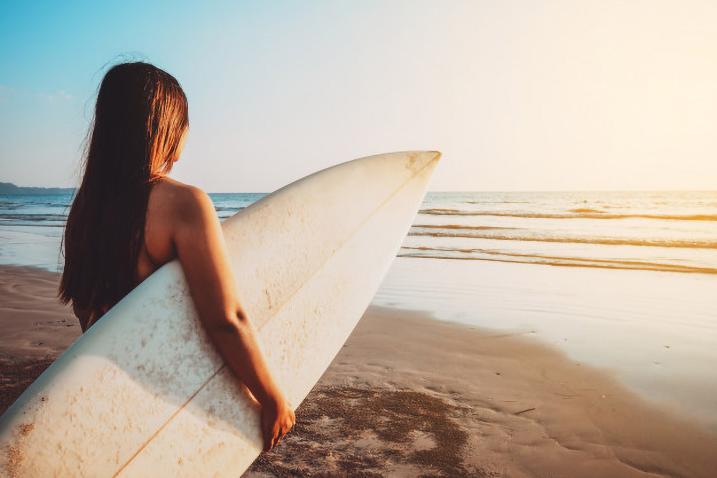 Image of a teen staring at the ocean holding a surfboard